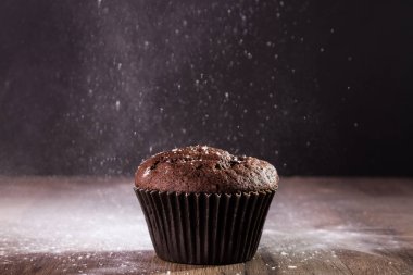 Pudra şekeri ile siyah bir zemin üzerine çikolatalı muffin.