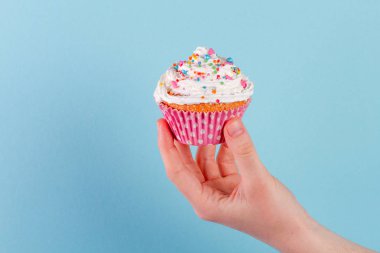 Muffin krema ve parlak toz ile parlak bir arka plan üzerinde tutan el 