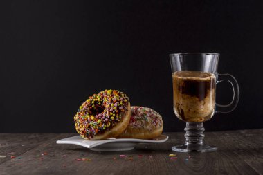 Çikolata, renkli donut ahşap bir masa üzerinde beyaz bir plaka üzerinde yalan. Bir kapuçino yanında, bu.