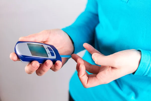 Midsection view of diabetic girl using blood glucose monitor on white background