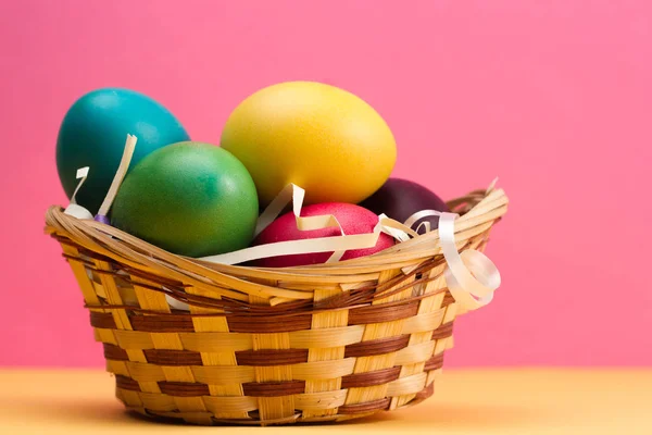Easter basket filled with Easter Eggs on table over a pink background