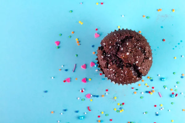 Chocolate muffin on a blue background with powdered sugar
