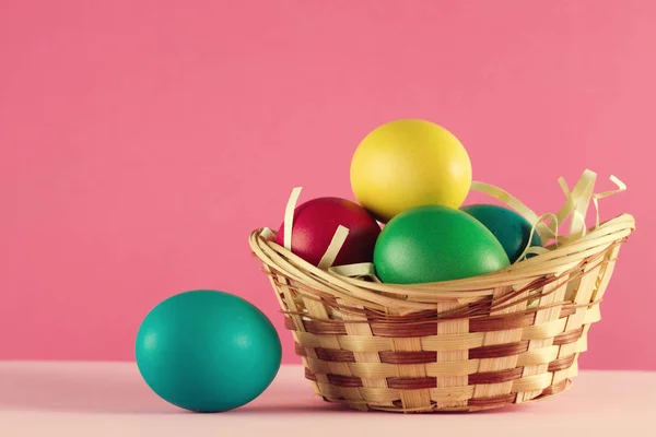 Easter basket filled with Easter Eggs on table over a pink background
