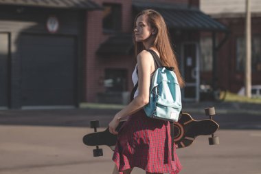 Kız longboard ve şehirde yürüyüş sırt çantası ile kırmızı gömlekli