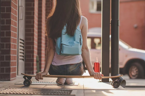 ロングボードの上に座ってブルー バックパックを持つ少女の背面図 — ストック写真