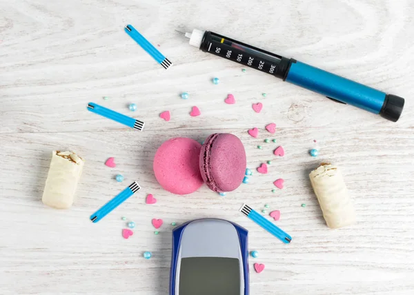 Frame for text from sweet macaroons, insulin pen, glucometer, blood sugar check strips, chocolate bar and sweet powder on wooden white background