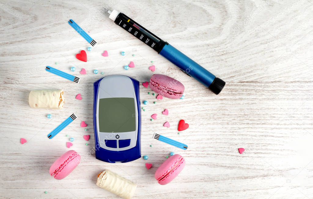 Frame for text from sweet macaroons, insulin pen, glucometer, blood sugar check strips, chocolate bar and sweet powder on wooden white background