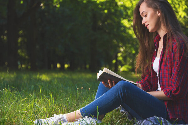 молодая женщина читает книгу в парке в дневное время
