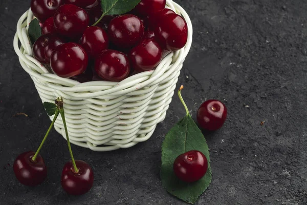 White basket with ripe cherries on black background.