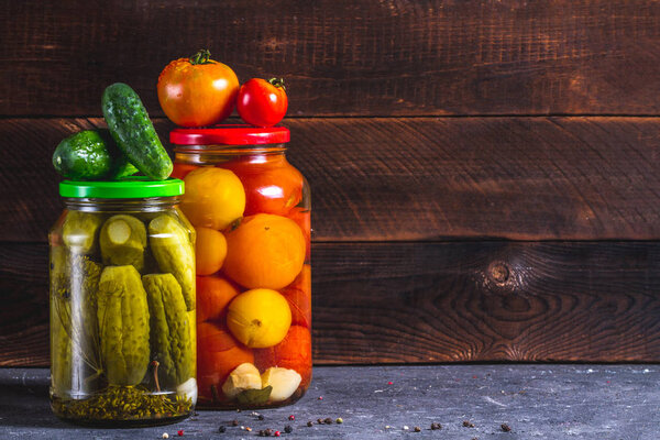 Jars of pickles homemade, fresh cucumbers and tomatoes on a dark, wooden background. Copy space. Stock of food