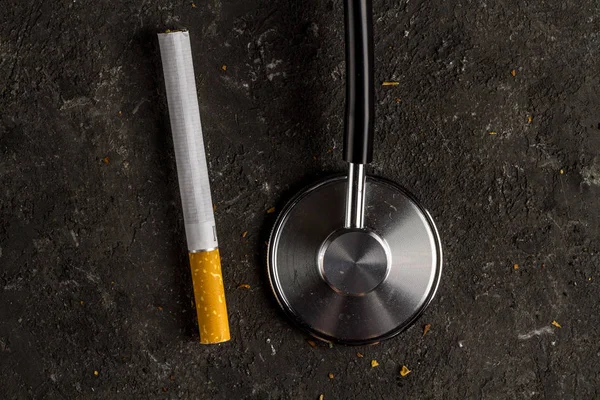 Nicotine, tobacco addiction. Harmful, unhealthy habit. Cigarette and stethoscope on a black background. Medical assistance to dependent people