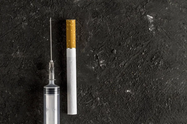 The concept of combating smoking, fighting with nicotine addiction. Cigarette and medical syringe for injections on a dark background. Drug addiction