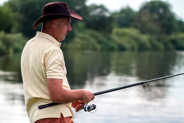 A fisherman in shorts and hat is fishing on the shore of the lake