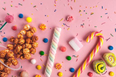 Renkli, çocuk, sağlıksız şeker, reçel, hatmi, karamelli patlamış mısır, chupa chups pembe bir arka plan üzerinde. Bir sehpa dolusu şeker. Üstten görünüm