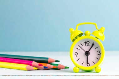 Sabahın erken saatlerinde okula çalar saat tarafından uyan. Okul hayatı. Çalar saat ve mavi bir arka plan üzerinde renkli kalemler. Okul kavramı