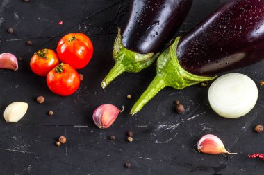 Taze patlıcan, kırmızı domates, sarımsak, soğan ve siyah bir zemin üzerine baharat. Taze sebze 