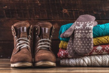 Kazak örme, kış, katlanmış, sıcak eldiven ve kış botları bir ahşap zemin üzerinde. Kış giysileri. Çirkin Noel kazağı. Sıcak, rahat giysiler