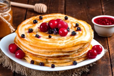 Yaban mersini ve kiraz, frambuaz reçeli, süt ve bal ahşap arka plan üzerinde taze çilek ile krep. Lezzetli, sağlıklı kahvaltı