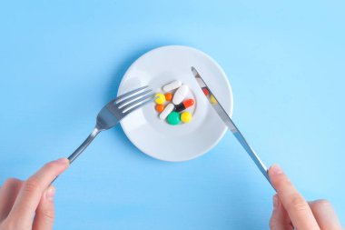 Tıp kavramı, hap kavramı. İlacı. Çok renkli tablet, kapsül, ilaç, çatal ve bıçak üzerinde mavi bir arka plan ile plaka