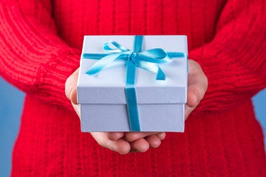 Küçük beyaz hediye kutusu tutan eller mavi kurdele ile sarılmış. Sevdiklerinize armağanlar almak ve vermek için. 