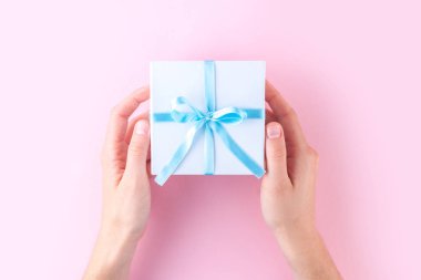 Küçük beyaz hediye kutusu tutan eller mavi şerit üzerinde pembe bir arka plan ile sarılmış. Sevdiklerinize armağanlar almak ve vermek için. 