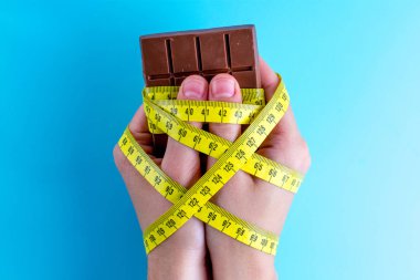 Diyet kavramı. Ağırlık kavramı kaybetmek. Sarı mavi bir arka plan kasette ölçme ile çikolata elinde bağlı. 