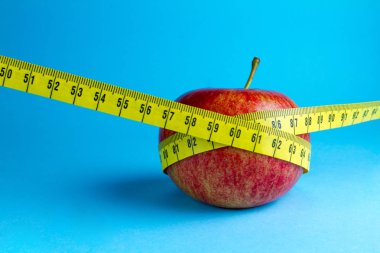 Diyet kavramı. Ağırlık comcept kaybetme. Sarı ölçüm bandı ve mavi bir arka plan üzerinde bir elma.
