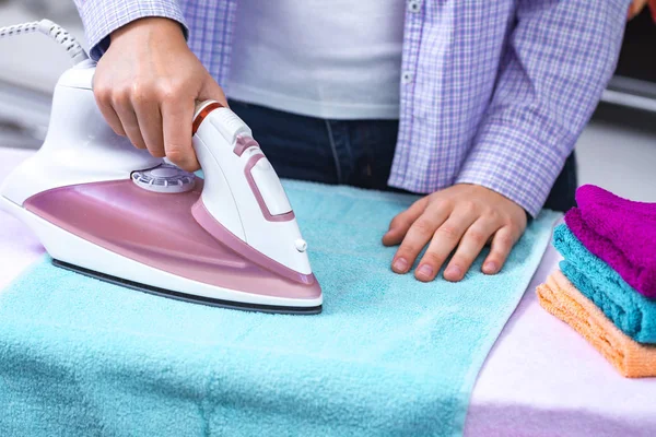 A young woman ironing clean linen on the ironing board with iron. Ironing clothes and laundry