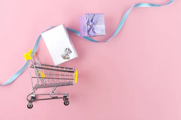 Shopping cart and gifts on a pink background. Shopping concept. Discounts and sales. Buy gifts and goods. Top view. Copy space