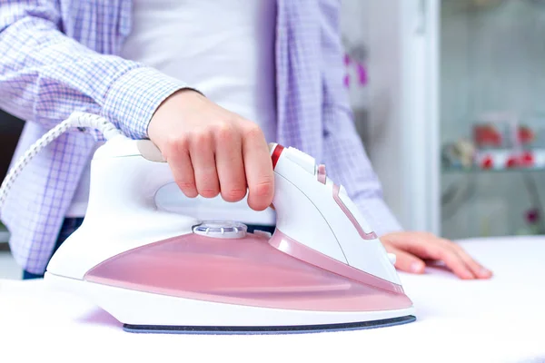 A young woman ironing clean linen on the ironing board with iron. Ironing clothes and laundry