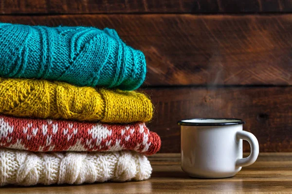 Winter, knitted sweaters and a mug of hot cocoa on a wooden background. Winter clothes. Ugly Christmas Sweater