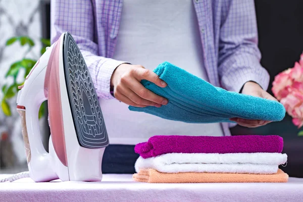 A young housewife in a shirt folds clean towels after ironing on the ironing board. Home routines. Ironing clothes and laundry