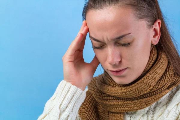 A young woman in a knitted scarf and a warm pullover feels bad, has a headache, a migraine. Weakened immunity. Treatment of colds and flu. Treatment of migraine.