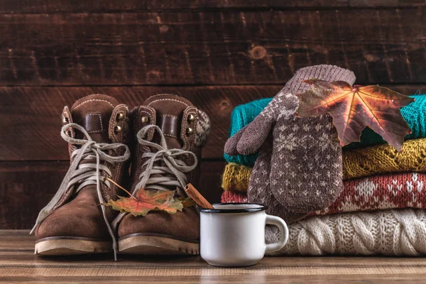 Knitted, folded sweaters, warm mittens, winter boots and autumn, maple leaves on a wooden background. Winter and autumn clothes. Ugly Christmas Sweater. Warm, comfortable clothes