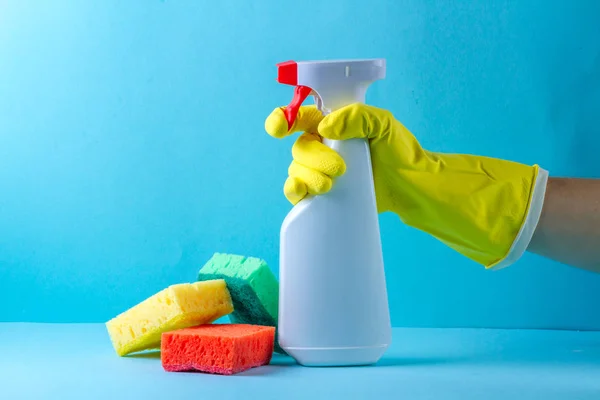 Spray for washing windows in hand and sponges for washing dishes on a blue background. Cleaning concept