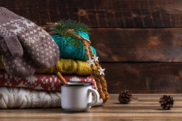 Winter, knitted, folded sweaters, warm mittens and a mug of hot cocoa with cinnamon on a wooden background. Winter and autumn clothes. Ugly Christmas Sweater