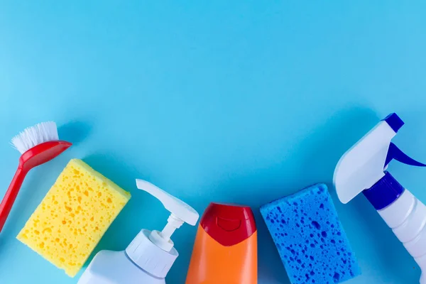 Bottles, sprays for cleaning the house, colored sponges for washing dishes and a brush on a blue background. Cleaning products, copy space. Top view