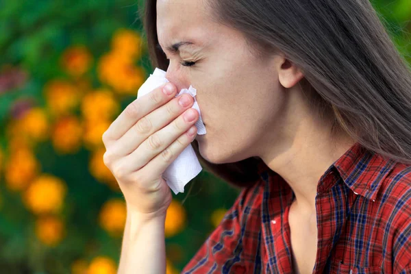 Allergy to flowering. Sneezing and runny nose from pollen. Allergic reactions. A woman in the park holds a handkerchief and sneezes from the bloom of flowers and pollen