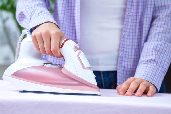 A young woman ironing clean linen on the ironing board with iron.