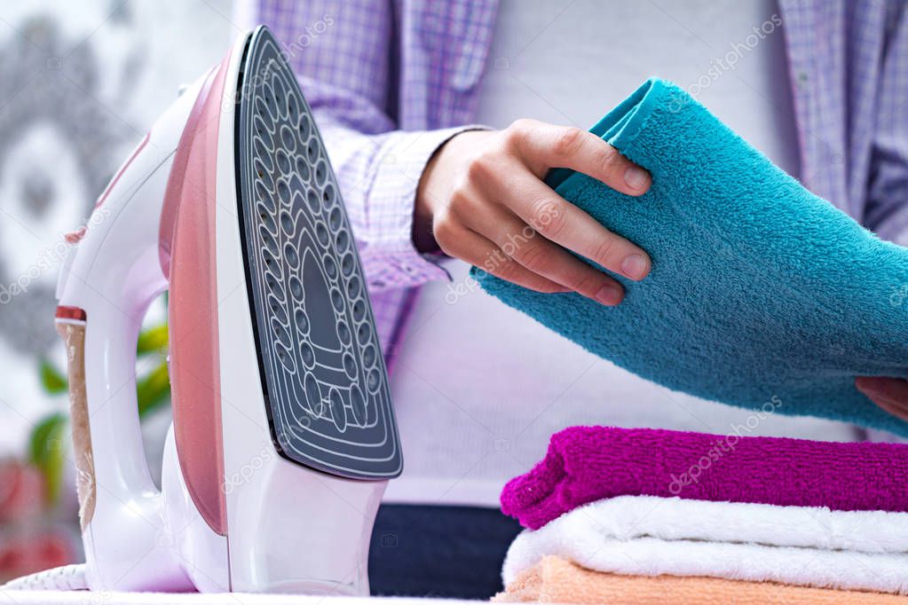 A young housewife in a shirt folds clean towels after ironing on the ironing board. Home routines. Ironing clothes and laundry