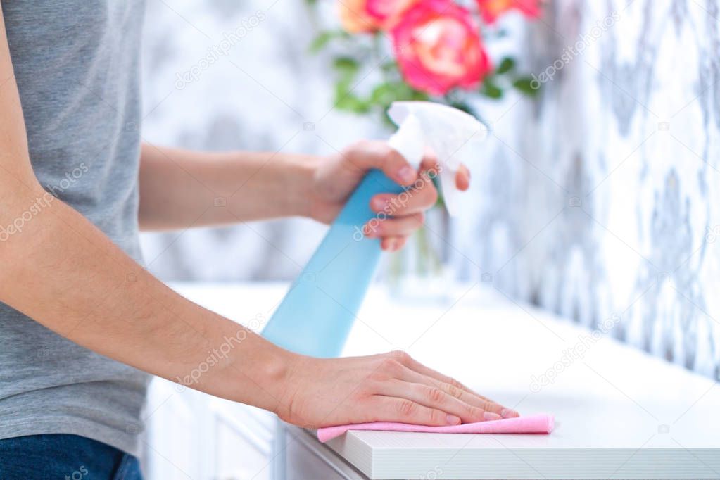 A young woman wipes the dust with a rag and spray in the room. House cleaning