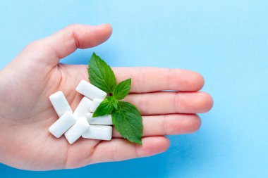 Mavi bir arka plan üzerinde bir elinde taze nane bir parça sakız. Taze bir nefes, naneli sakız