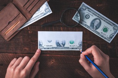 Counterfeiter forges banknotes. Fake concept. Fake money, a wallet with American dollars, a magnifier on a wooden background. Top view  clipart