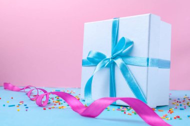 Gift, small box tied with a satin blue ribbon on a pink background. Gift concept. Surprises and gifts for loved ones, congratulations on holidays, give gifts. Copy space  clipart