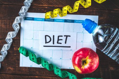 Drawing up and planning a program of sports training and diet. Sports and healthy lifestyle. An apple, a bottle of water, a measuring tape on a wooden background. Motivation. Sport and diet concept 