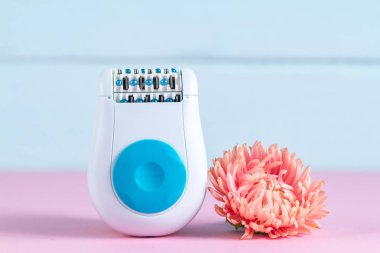 Epilatör ve mavi bir arka plan üzerinde pembe bir çiçek. Depilatory. İstenmeyen saç kaldırılması. Spa ve erkek tedavileri. Epilasyon kavramı