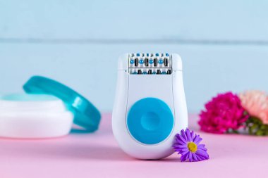 Epilatör, krem ve mavi bir arka plan üzerinde çiçekler. Depilatory. İstenmeyen saç kaldırılması. Spa uygulamaları 