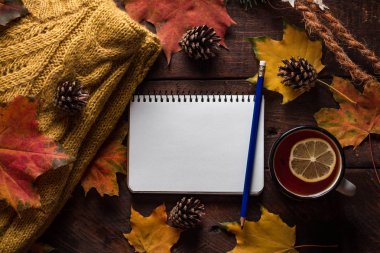 Sıcak, örgü kazak, çam kozalakları, bir fincan sıcak çay limon ve sonbahar akçaağaç yaprakları ahşap arka plan üzerinde. Sonbahar giysileri. Kopya alanı