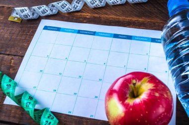 Spor eğitimi ve diyet programı hazırlıyor ve planlıyor. Spor ve sağlıklı yaşam tarzı. Bir elma, bir şişe su, ahşap arka plan üzerinde bir ölçüm bandı. Spor ve diyet konsepti 