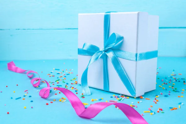 Gift, small box tied with a satin blue ribbon on a blue background. Gift concept. Surprises and gifts for loved ones, congratulations on holidays, give gifts
